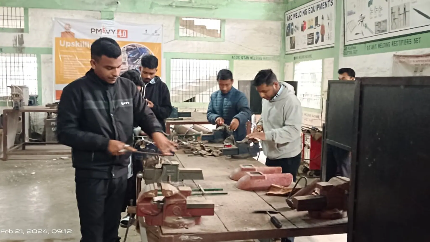 A welding workshop floor with equipment laid out and trainees at the benches