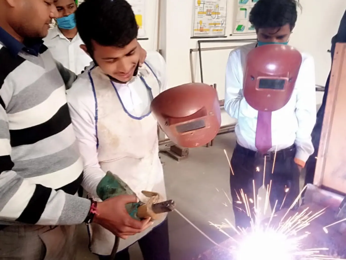 A trainee arc welding under supervision as sparks fly, classmates watching in welding masks